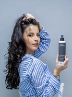 Зареди изображението в галерията, Жена с къдрави коси държи F-Expert спрей за обем 250 мл, с усмивка, на сива стена.