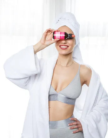 Млада жена с бял халат и кърпа на главата, държи продукт за коса, промотиращ Против косапад / Растеж на косата.